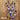 Blue Sunbathing Mini Bikini crochet two-piece with white daisies and tassel ties on a wooden deck.